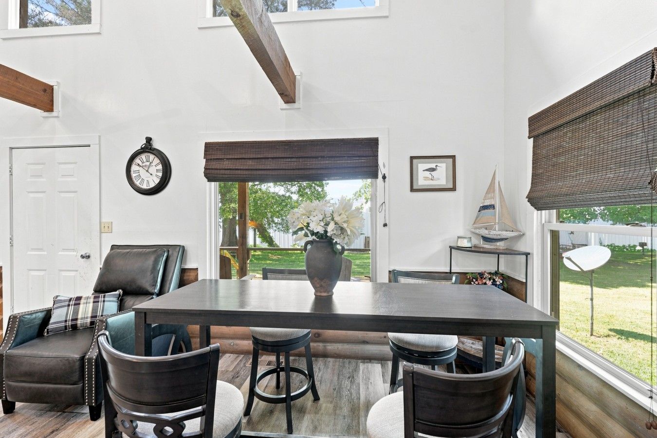 Un coin repas comprenant une table en bois, quatre chaises, une horloge et une fenêtre donnant sur l’extérieur.