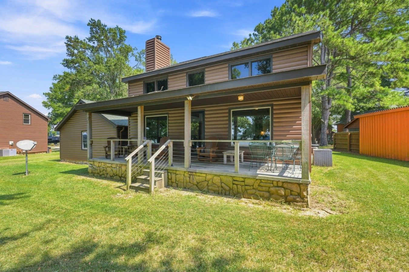 A two-story house with a stone foundation, a covered porch with outdoor seating, and a chimney.