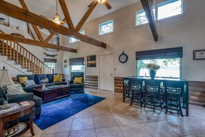 A spacious living room with a staircase, wooden beams, a dining area with chairs, and a large window. - Scenic Solitude - Doublehead (Town Creek)