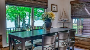 A dining area with a table, chairs, a vase with flowers, a sailboat model, and a view of trees and water.