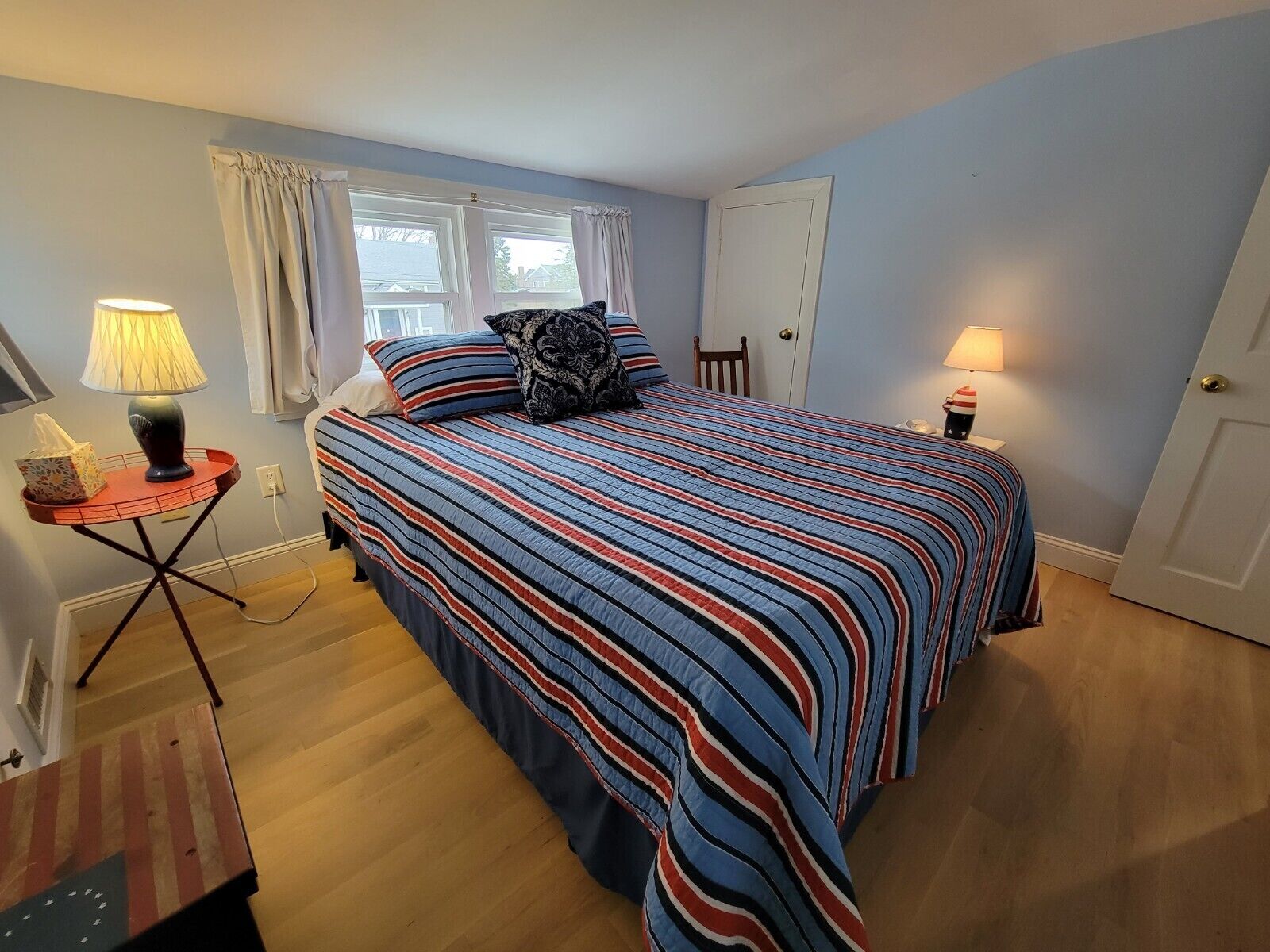 Une chambre à coucher avec un lit, deux tables de chevet, une lampe, une fenêtre avec des rideaux et une porte.