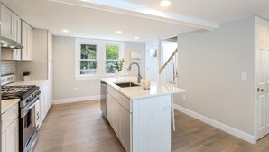 A modern kitchen with white cabinetry, a central island, and a window with a view of greenery. - Sprawling 5 BR Chatham Escape / Endless Outdoor Living & Entertaining Choices (Chatham)