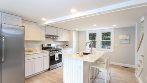 A modern kitchen with white cabinetry, a stainless steel refrigerator, a gas stove, and a sink with a window above it. - Sprawling 5 BR Chatham Escape / Endless Outdoor Living & Entertaining Choices (Chatham)