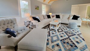 A spacious living room with a high ceiling and exposed wooden beams, featuring a grey sofa set, a patterned rug, and a white coffee table. - Sprawling 5 BR Chatham Escape / Endless Outdoor Living & Entertaining Choices (Chatham)