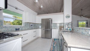 A modern kitchen with white cabinets, a stainless steel refrigerator, and a large island with a sink. - Newly Remodeled Home on Calm Caribbean w/Sunset Views, Snorkeling, Generator! (N Palmetto Point)