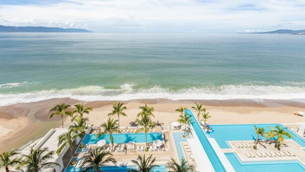 Un resort con piscina, palmeras y vista a la playa.
