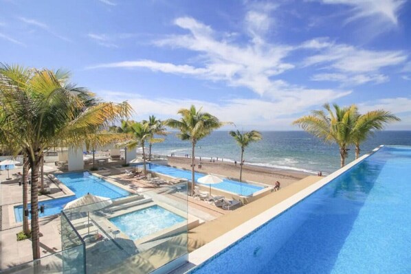 Relax by the oceanfront pool, surrounded by palm trees and a separate hot tub area.