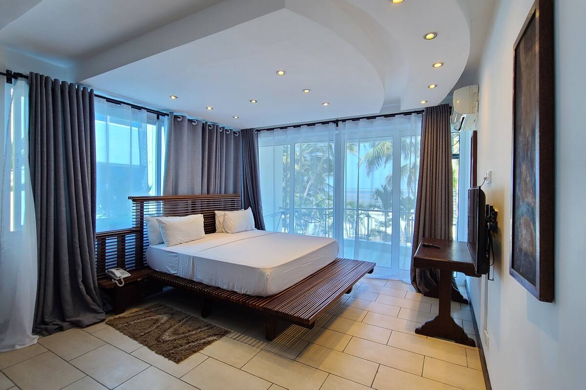 A bedroom with a large bed, a bedside table, a TV, and a view of the outdoors.