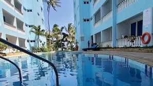 A swimming pool with clear blue water, surrounded by light blue buildings with balconies. - c3 Cowrie Shell Residences (Mombasa)