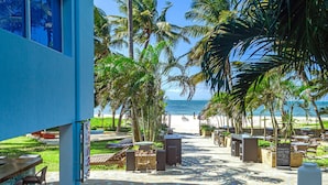 A beachside resort with a paved walkway leading to the beach, palm trees, and outdoor seating areas. - c3 Cowrie Shell Residences (Mombasa)