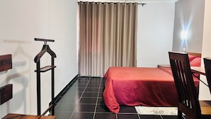 Una camera da letto piccola e ordinata, con un letto, una sedia, una scrivania e un appendiabiti.