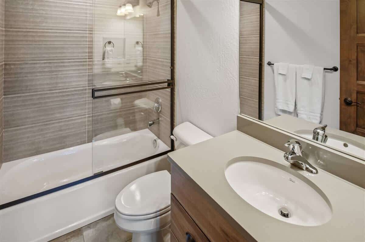 Ett modernt badrum med en duschavdelning med glasväggar, en vit toalett, ett beige handfat med tillhörande skåp och en stor spegel.