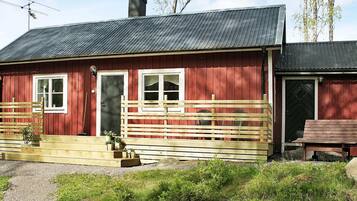 A red wooden house with a metal roof, a front porch with a wooden railing, and a chimney.