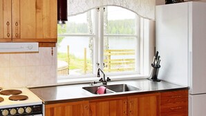 A kitchen with wooden cabinets, a stove, a sink, and a window with a view of a wooden dock and trees. - 7 Person Holiday Home in Skyllberg (Skyllberg)