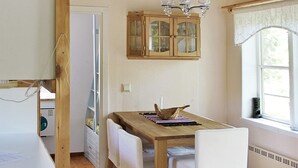 A dining area with a wooden table, white chairs, a chandelier, and a window with curtains. - 7 Person Holiday Home in Skyllberg (Skyllberg)