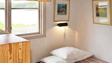 A small, single-bed room with a window, a wall-mounted light, and two framed pictures.