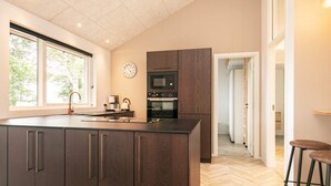 A modern kitchen with dark cabinetry, a built-in oven, and a large island with a sink. - 5 Star Holiday Home in Millinge (Millinge)