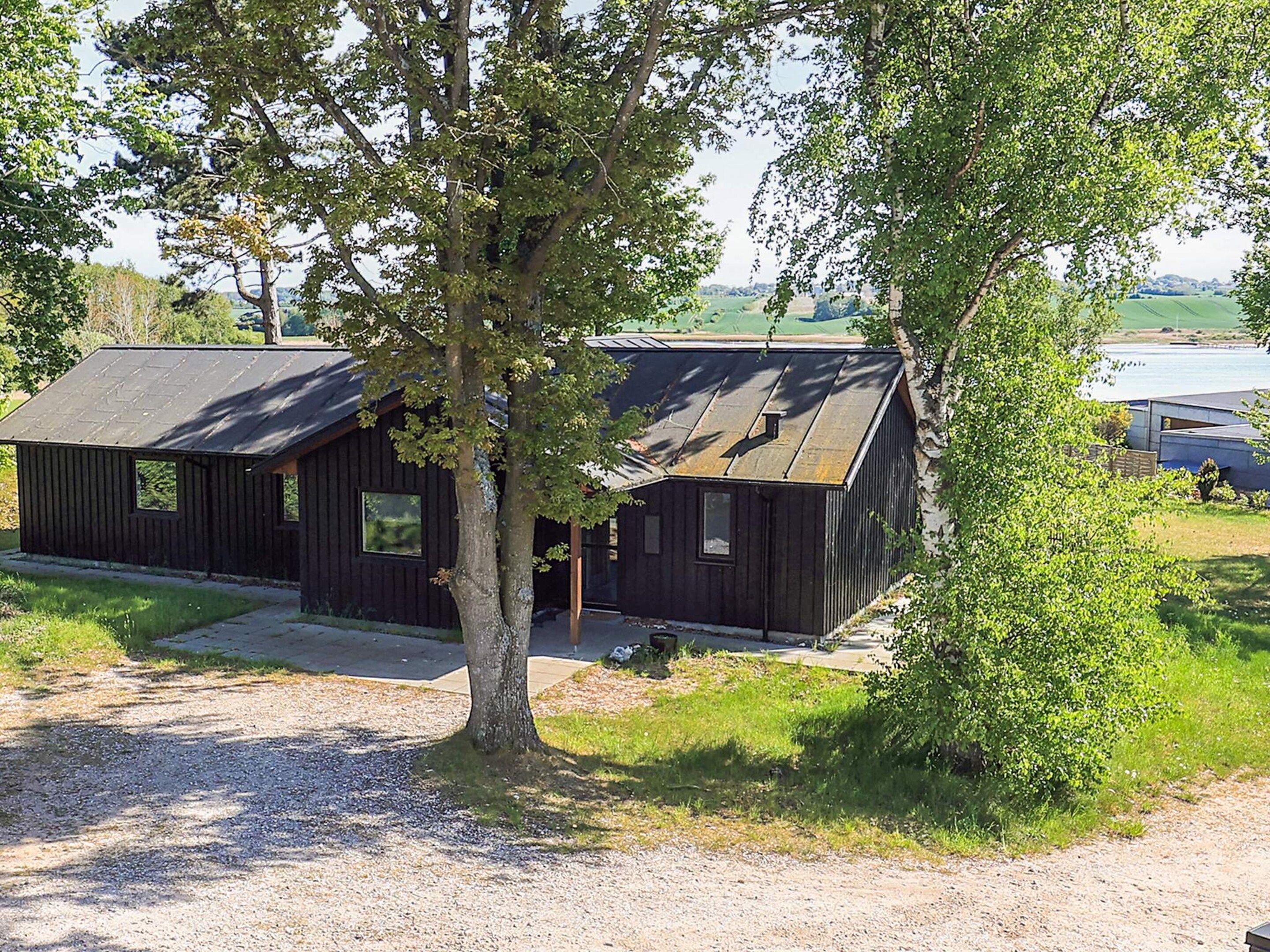Un chalet rustique avec une allée en gravier, entouré d’arbres et offrant une vue sur un lac.