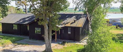 Un chalet rustique avec une allée en gravier, entouré d’arbres et offrant une vue sur un lac.