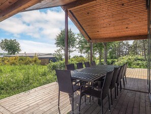 An outdoor wooden deck with a table and chairs, surrounded by greenery and a view of the sky. - 5 Star Holiday Home in Millinge (Millinge)