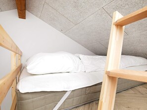 A small, single-bed room with a sloped ceiling and a wooden bunk bed structure.