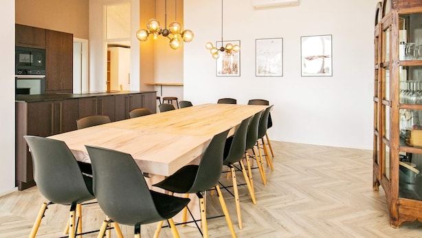 A dining area with a wooden table and chairs, a kitchen in the background, and a wooden cabinet with glass doors. - 5 Star Holiday Home in Millinge (Millinge)