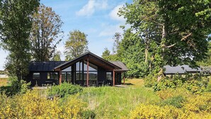 A modern house with a large glass facade, surrounded by lush greenery and yellow flowers. - 5 Star Holiday Home in Millinge (Millinge)