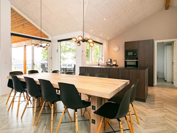 A modern kitchen with a wooden island, black chairs, and a large dining table. - 5 Star Holiday Home in Millinge (Millinge)
