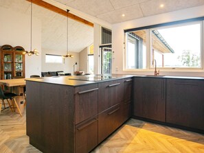 A modern kitchen with a large island, dark cabinetry, and a herringbone-patterned floor.