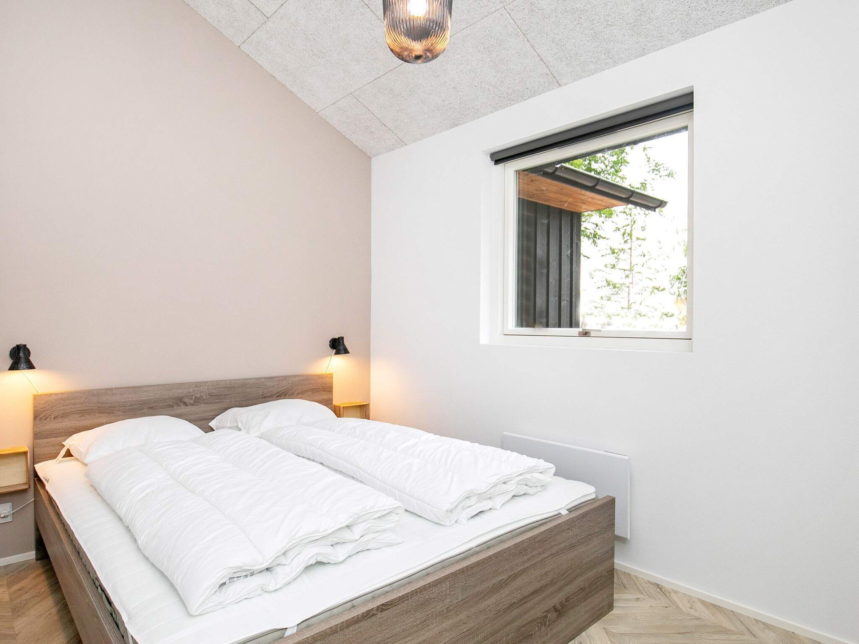 A modern bedroom with a wooden bed, two bedside lamps, a window with a view of greenery, and a ceiling light fixture.