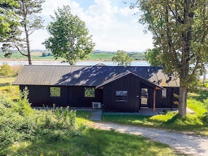 A rustic cabin with a metal roof, surrounded by greenery and a clear sky.