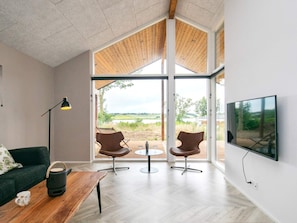 A modern living room with a large window, a flat-screen TV, and a wooden ceiling.