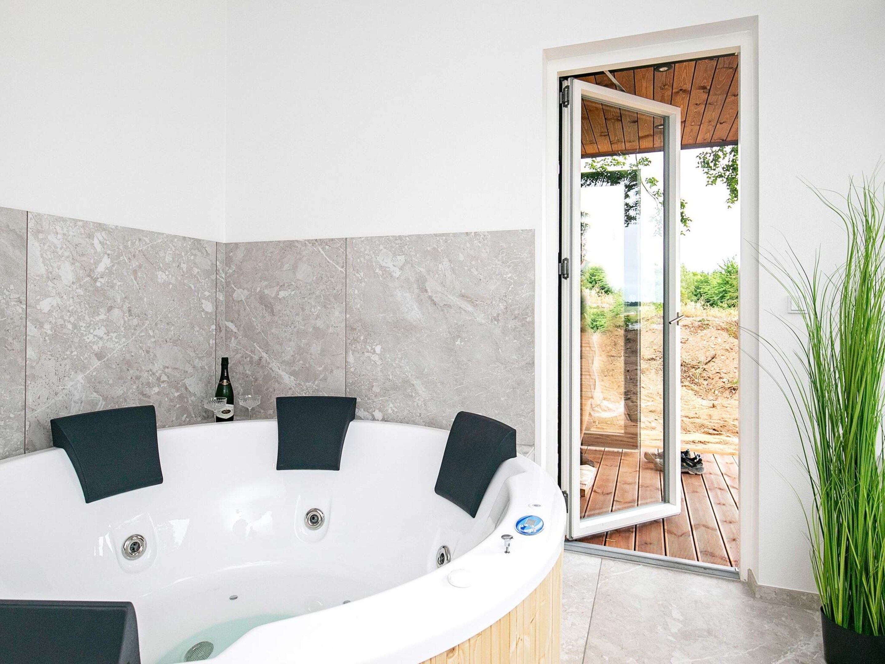 A modern bathroom with a freestanding bathtub, a glass door leading to an outdoor area, and a potted plant.