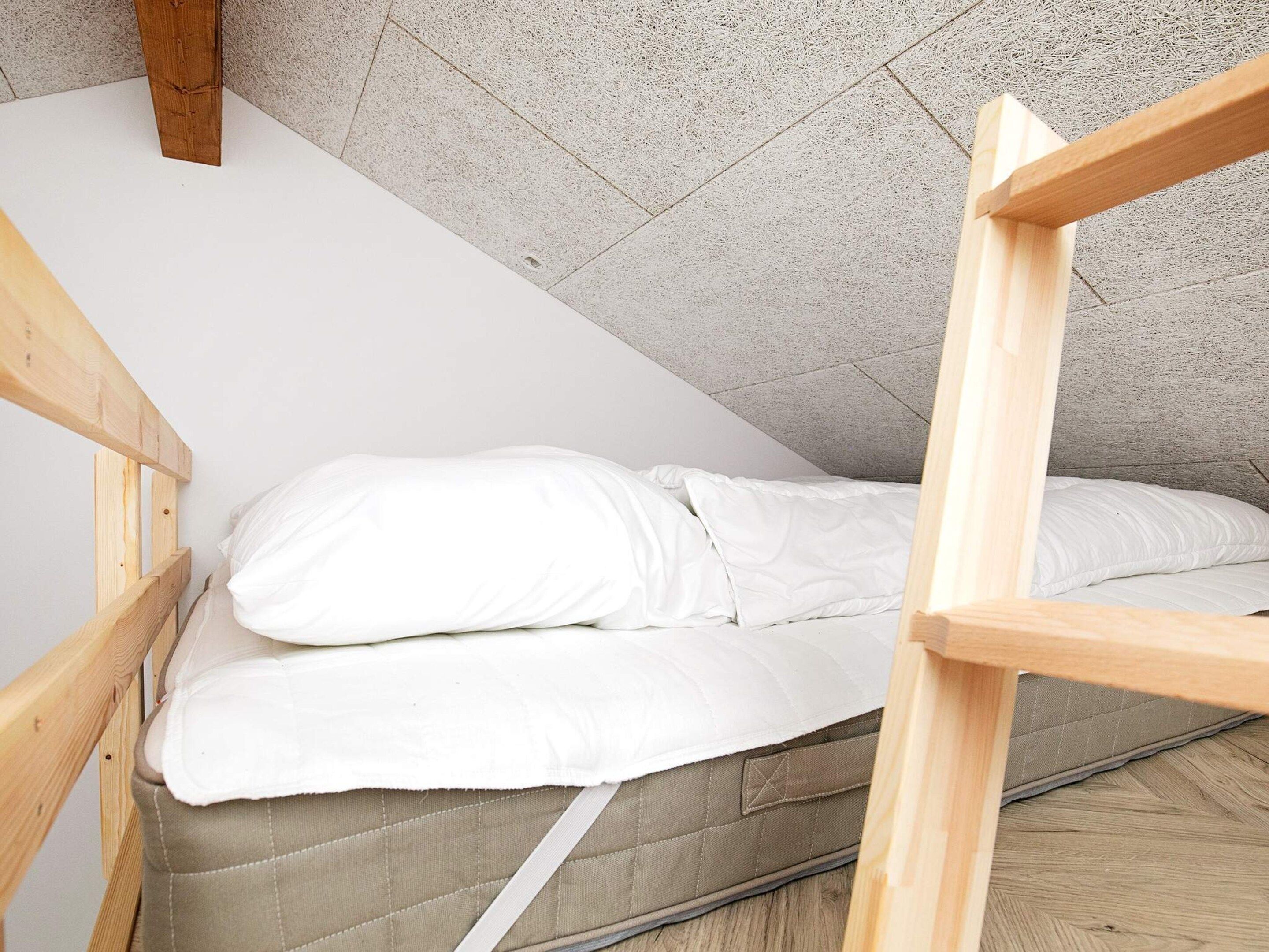 Ein kleines Zimmer mit einem einzelnen Bett, geneigter Decke und einem Bettgestell aus Holz.