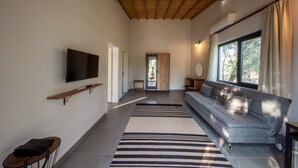 Uma sala de estar moderna com teto de madeira, uma TV de tela plana na parede, um sofá cinza, um tapete listrado e uma janela grande com cortinas.