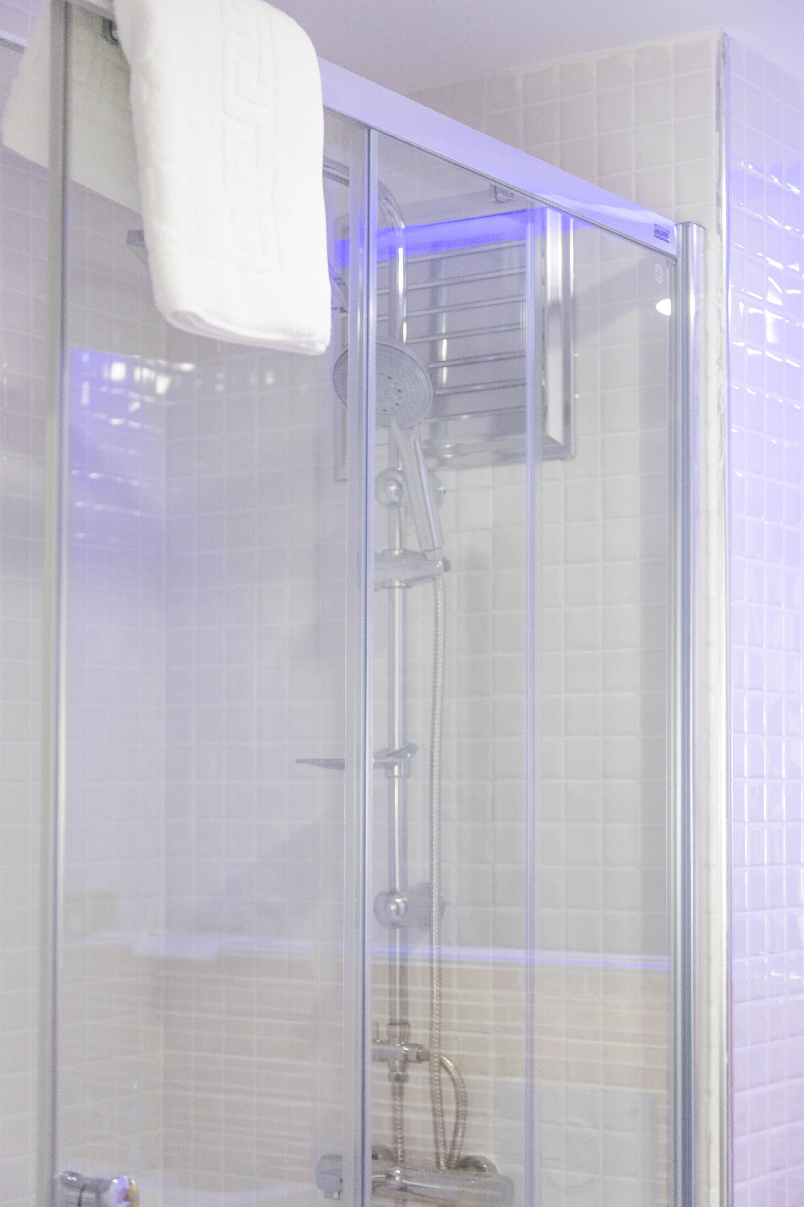 A glass-enclosed shower with a handheld showerhead and a towel hanging on the wall.