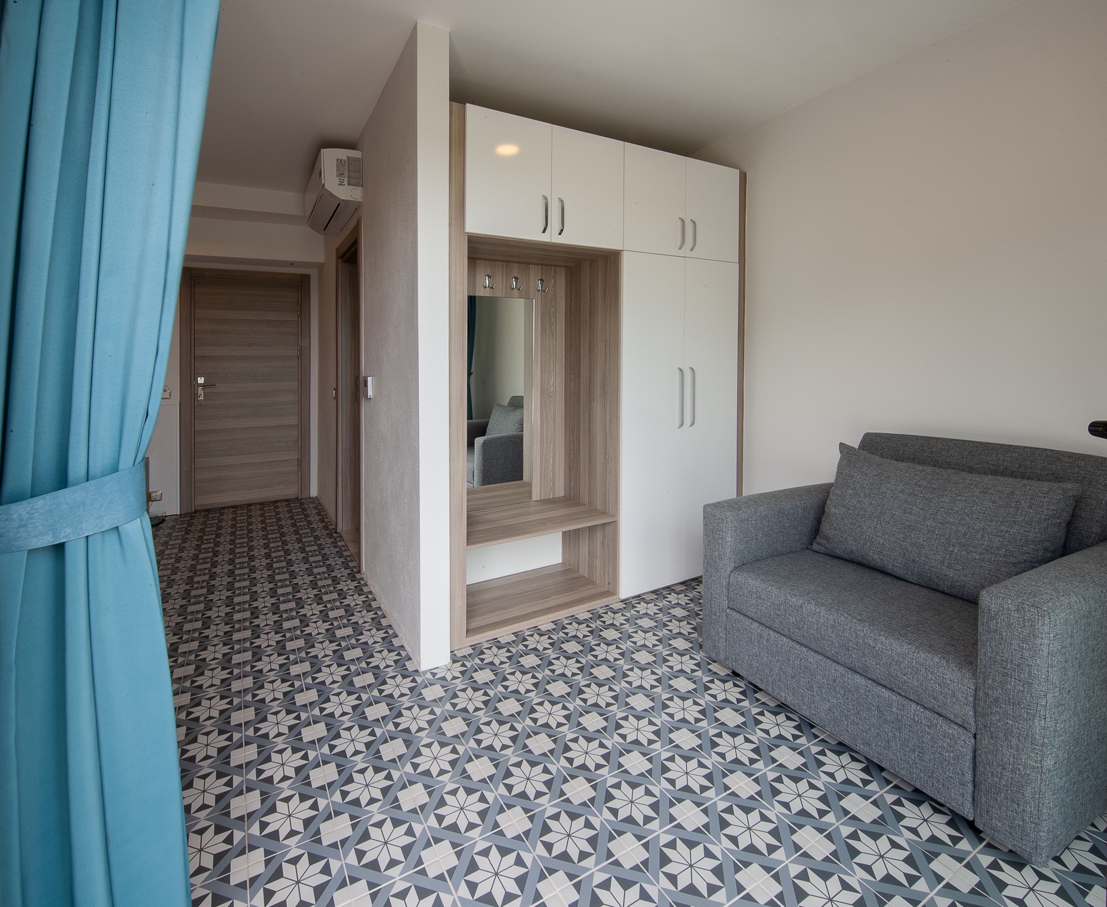 Una habitación con un sofá gris, un armario con puertas espejadas y un piso estampado.