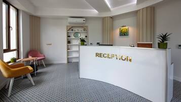 Una zona de recepción con un mostrador blanco, una silla rosa, una silla amarilla y un suelo estampado.