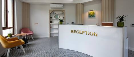 A reception area with a white reception desk, a pink chair, a yellow chair, and a patterned floor.