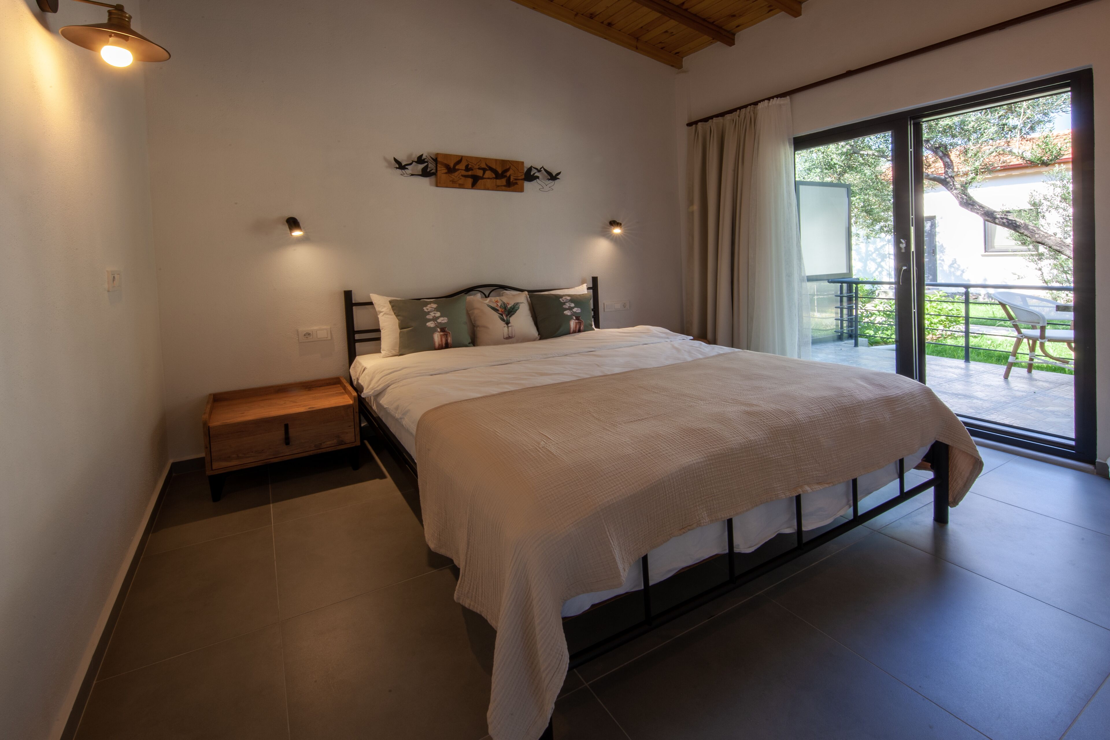 Quarto com uma cama grande, uma mesa de cabeceira de madeira, uma obra de arte na parede e uma porta de vidro deslizante para área externa.