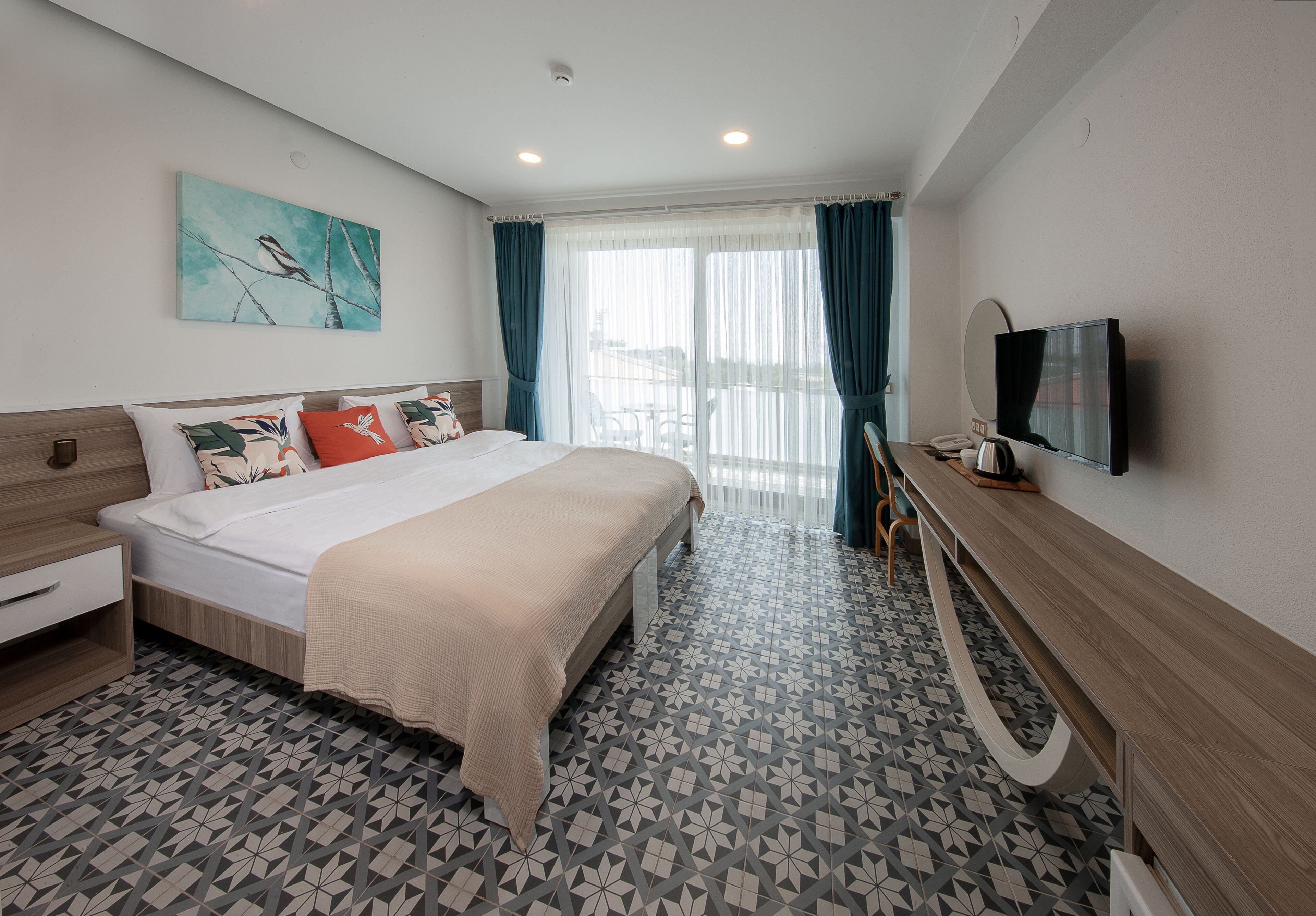 Una habitación de hotel moderna con una cama grande, un televisor de pantalla plana, un escritorio de madera y vistas al exterior a través de la ventana.