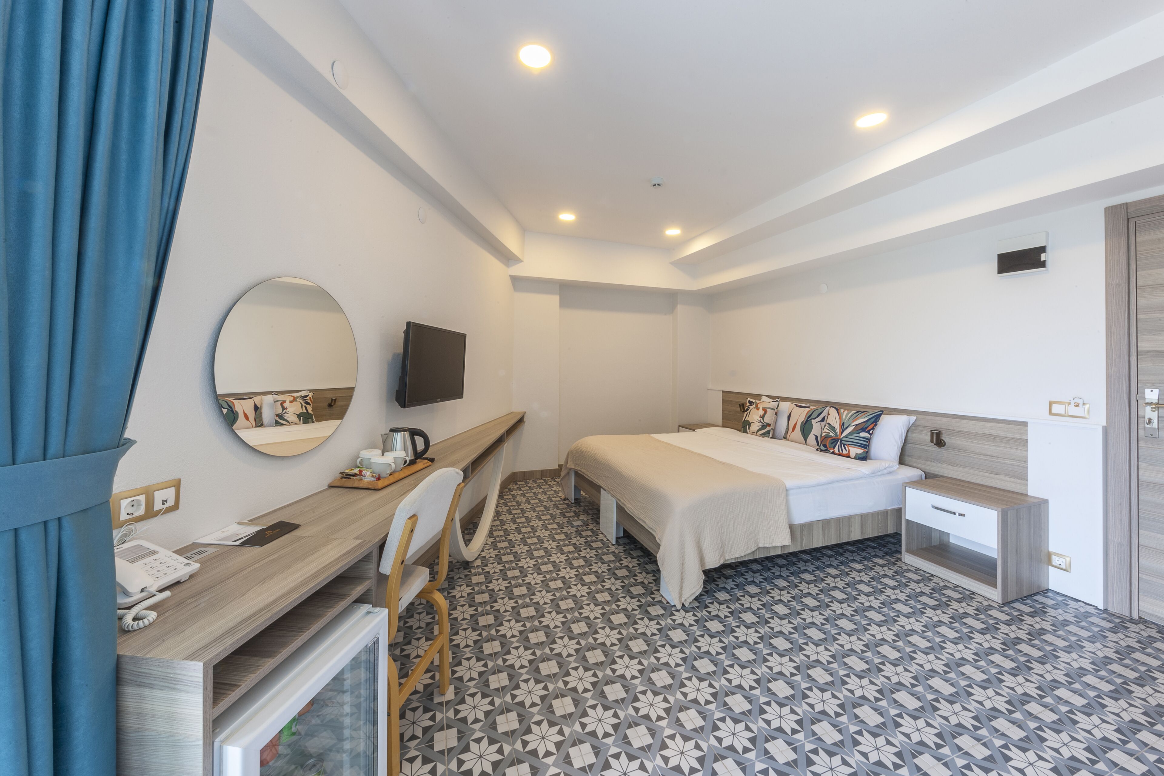 A hotel room with a bed, bedside table, desk, chair, and a television mounted on the wall.