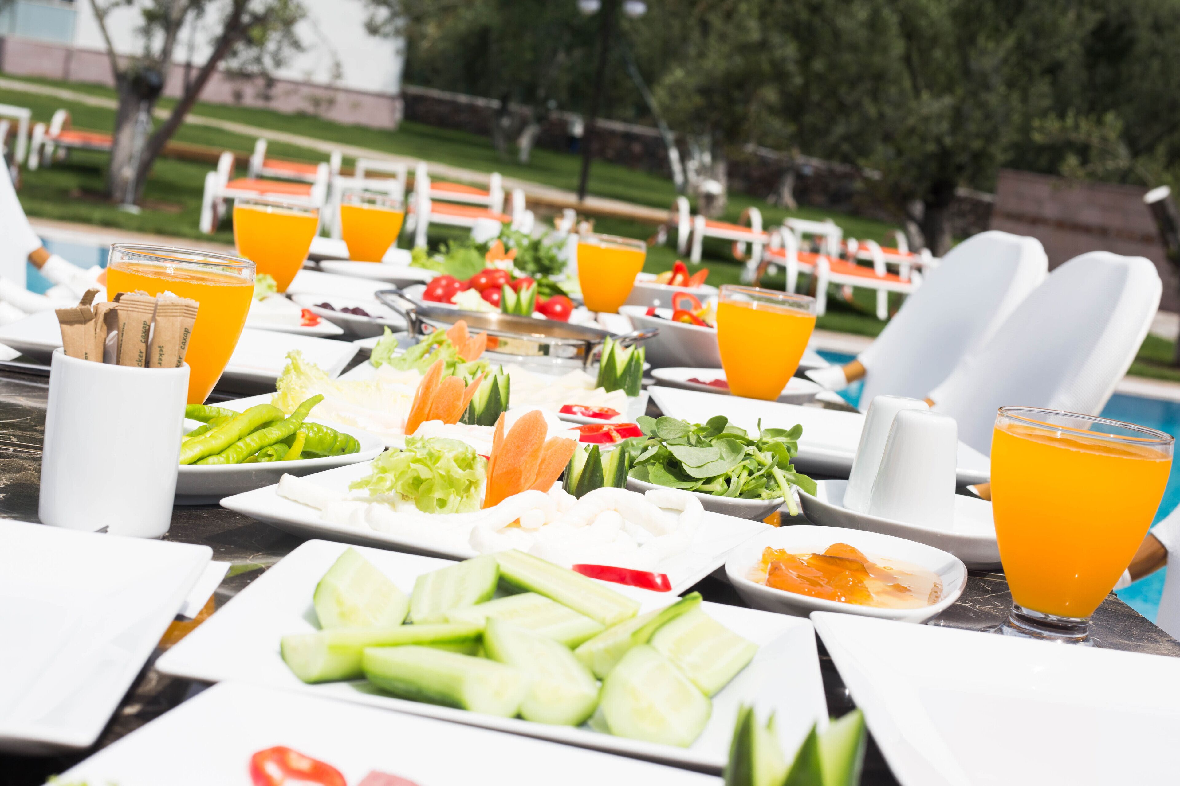 A table set for a meal with various dishes and drinks, overlooking a pool area.
