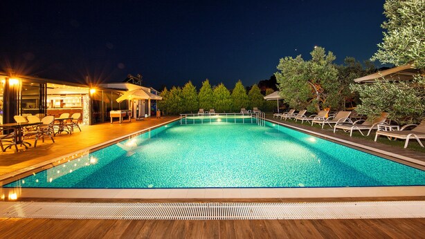 Uma área de piscina à noite, com espreguiçadeiras e um bar.