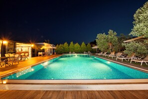 A nighttime swimming pool area with lounge chairs and a bar area.