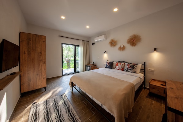 A bedroom with a large bed, a wooden wardrobe, a TV, and a sliding glass door to the outside.