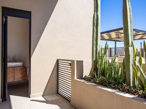 A modern outdoor space with a built-in planter, a door leading to a bathroom, and a large cactus plant. - Sea Esta is a ground-floor 2-BD, 2-BR condo within walking distance of downtown Cabo, the marina, and Cannery Beach. Featuring an open-concept living space, private balcony, and views of the city and the Sea of Cortez, it’s ideal for a relaxing Cabo. (Cabo San Lucas)