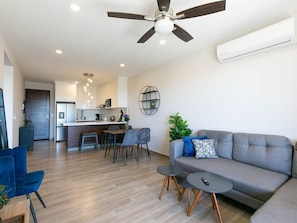 A modern living room with a grey sofa, two round tables, and a ceiling fan. - Sea Esta is a ground-floor 2-BD, 2-BR condo within walking distance of downtown Cabo, the marina, and Cannery Beach. Featuring an open-concept living space, private balcony, and views of the city and the Sea of Cortez, it’s ideal for a relaxing Cabo. (Cabo San Lucas)