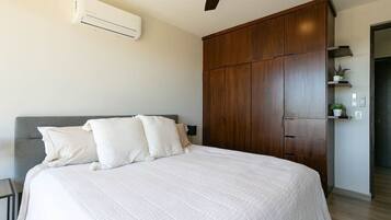A bedroom with a bed, a ceiling fan, a wardrobe, and an air conditioning unit.