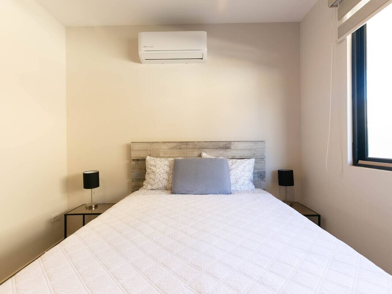 Une chambre à coucher comprenant un lit, deux tables de chevet, une tête de lit, un appareil de climatisation et une fenêtre.